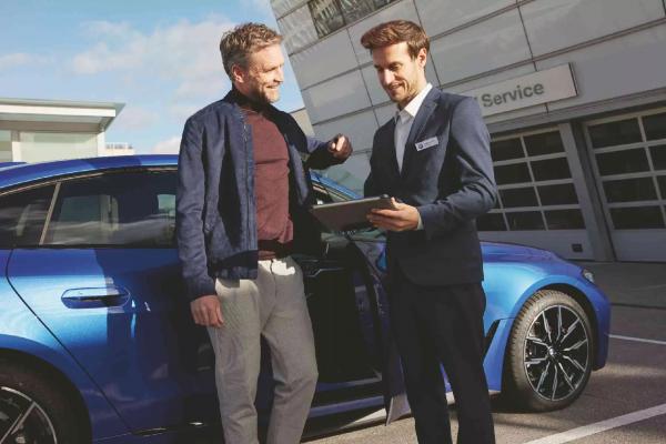 Ein Kundenberater einer BMW Servicewerkstatt erklärt einem Kunden die HU- und AU-Werte auf einem Tablet.