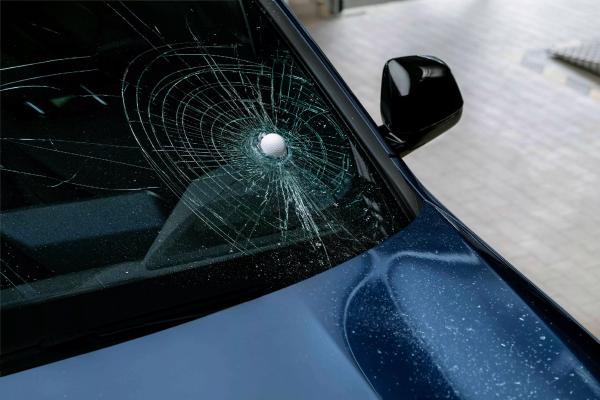 Ein BMW in der Werkstatt mit einem Glasschaden. Ein Golfball steckt in der Windschutzscheibe.