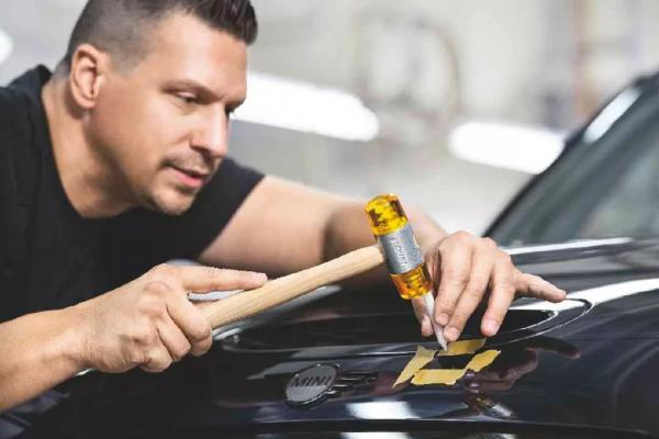 Ein Mitarbeiter einer MINI Service-Werkstatt korrigiert die Beulen im Lack eines schwarzen MINI Cooper S mit seinem Werkzeug.