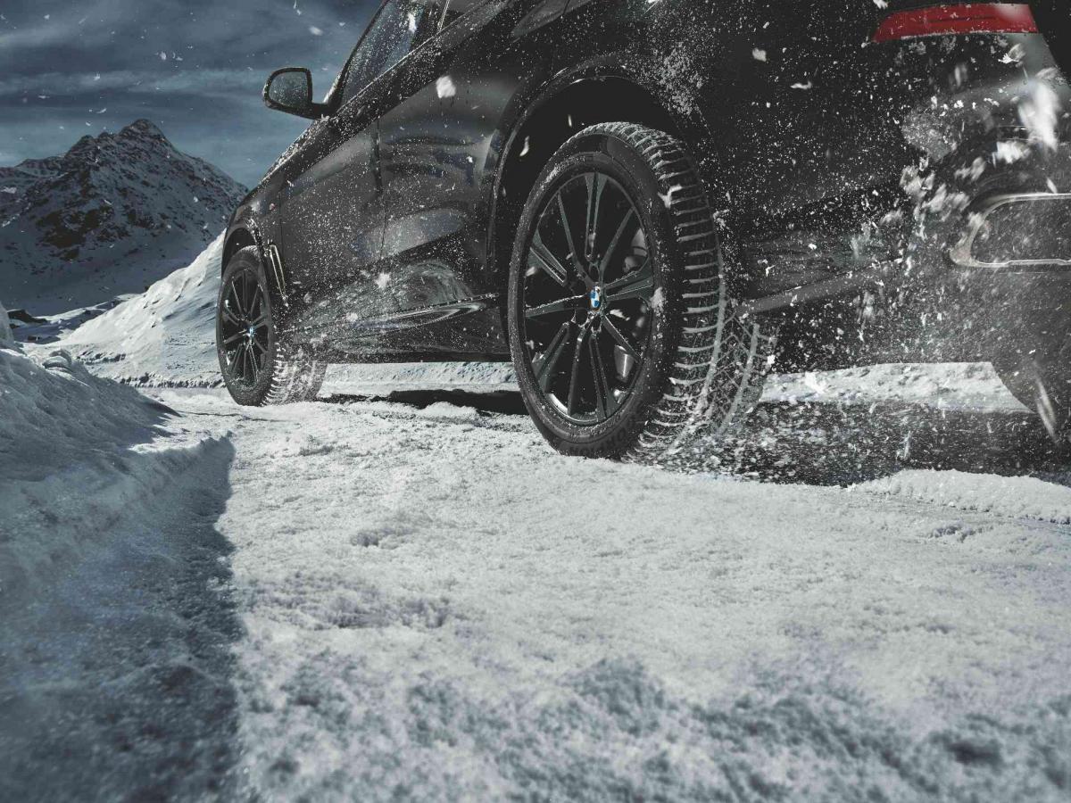 Die linke Seite eines BMW mit schwarzen Alufelgen im Schnee.