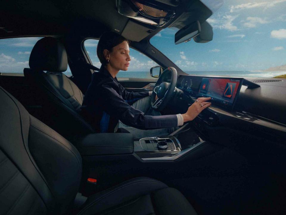 Eine Dame sitzt in einem BMW i7 und bedient das Infotainmentsystem über das Curved Display.