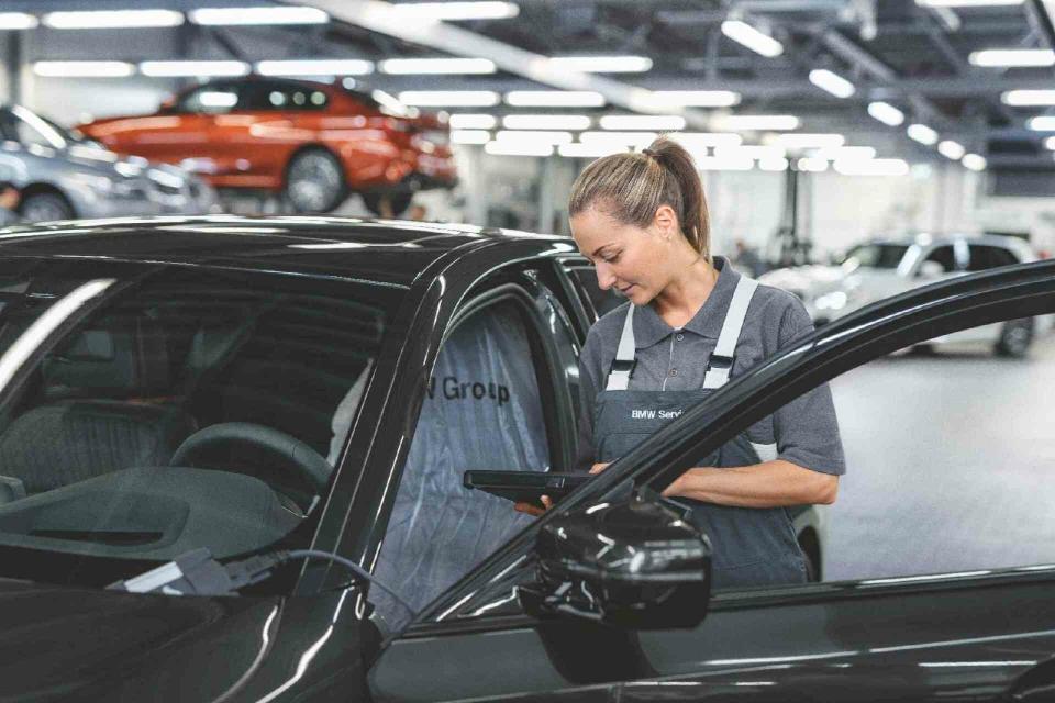 Die Mitarbeiterin einer BMW Werkstatt prüft den Fehlerspeicher eines schwarzen BMW.