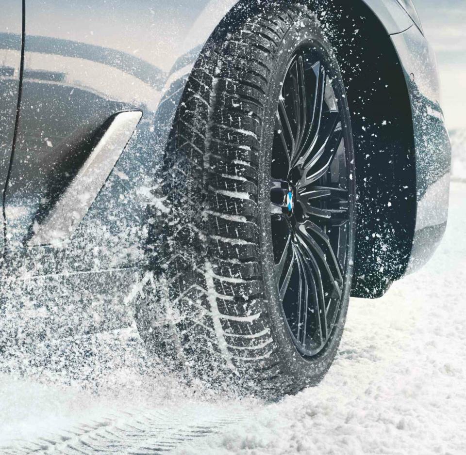 Der rechte Vorderreifen eines BMW mit schwarzer Alufelge im Schnee.