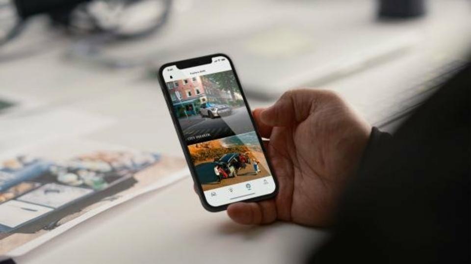 Ein Mann sitzt an seinem Computertisch und betrachtet die MINI App auf seinem Smartphone in der Hand.