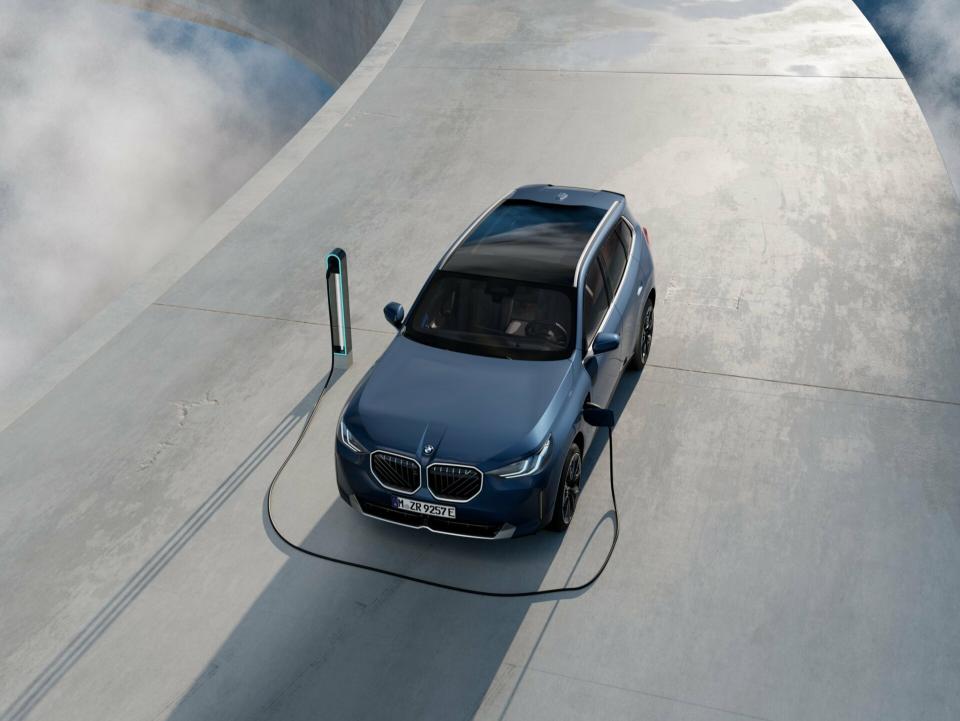 Ein BMW X3 30e xDrive Plug-in Hybrid in "Arctic Race Blue metallic" parkt an einer Ladestation im Sonnenuntergang.