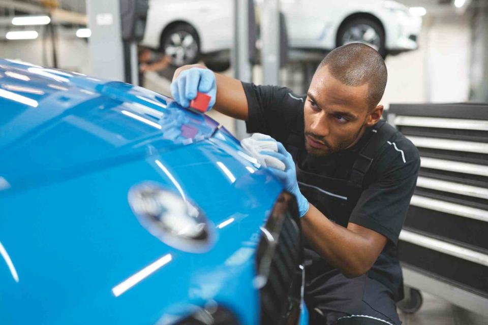 Ein Mitarbeiter in einer BMW Werkstatt untersucht einen Lackschaden, der mit Smart-Repair repariert wurde.