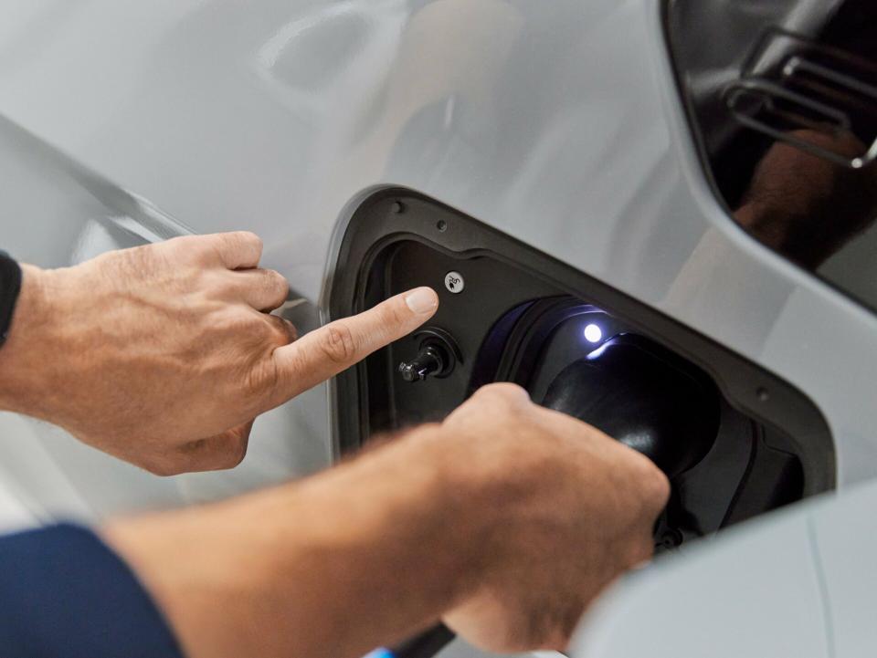 Eine Ladebuchse eines weißen BMW wird von einem Mann bedient. Er hält rechts einen Combo 2 Stecker für MODE 3.