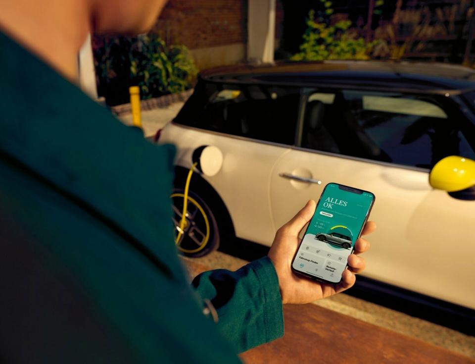 Ein Mann steht vor seinem ladenden MINI 3-Türer und bedient die MINI App auf seinem Smartphone.