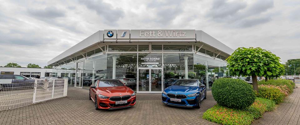 Der Eingang des Autohauses Fett & Wirtz in Moers mit zwei BMW Fahrzeugen davor.