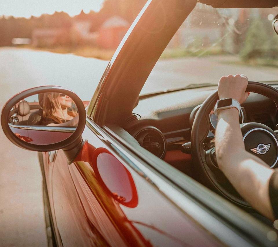 Eine junge Fahrerin steuert ihren roten MINI Cooper auf einer Straße in den Sonnenuntergang.