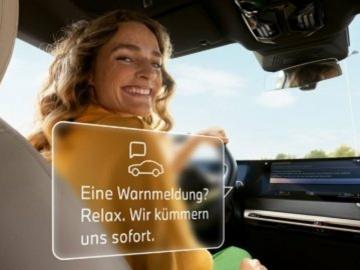 Eine glückliche Frau am Steuer eines BMW blickt nach hinten, während eine Meldung eingeblendet wird: 'Eine Warnmeldung? Relax. Wir kümmern uns sofort.'