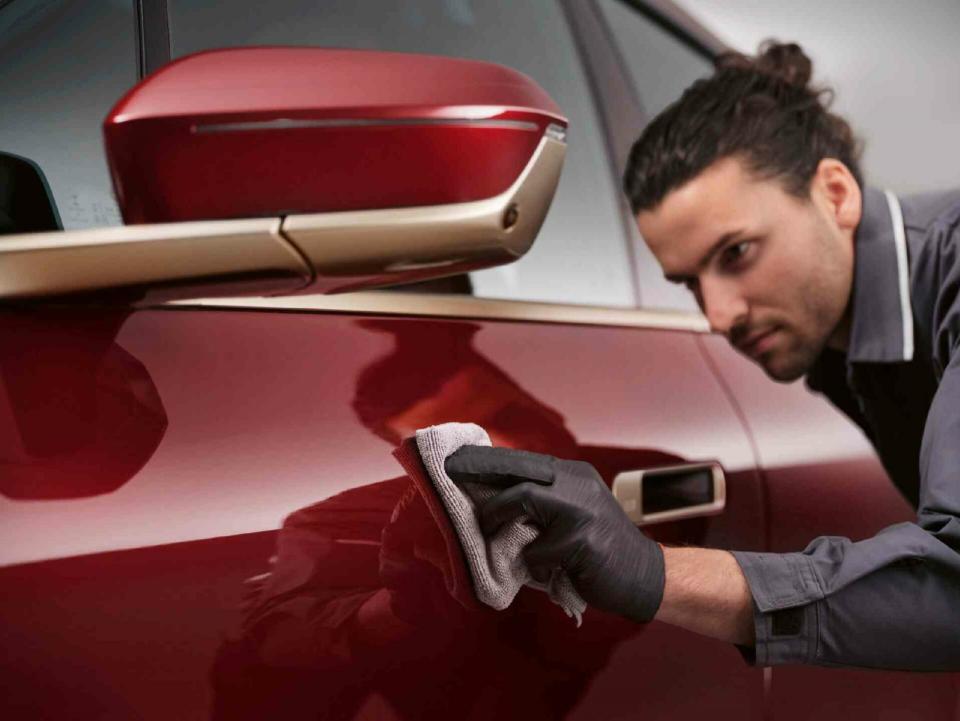 Ein Mitarbeiter einer MINI Servicewerkstatt poliert den Lack der Motorhaube eines roten MINIs mit einem Tuch.