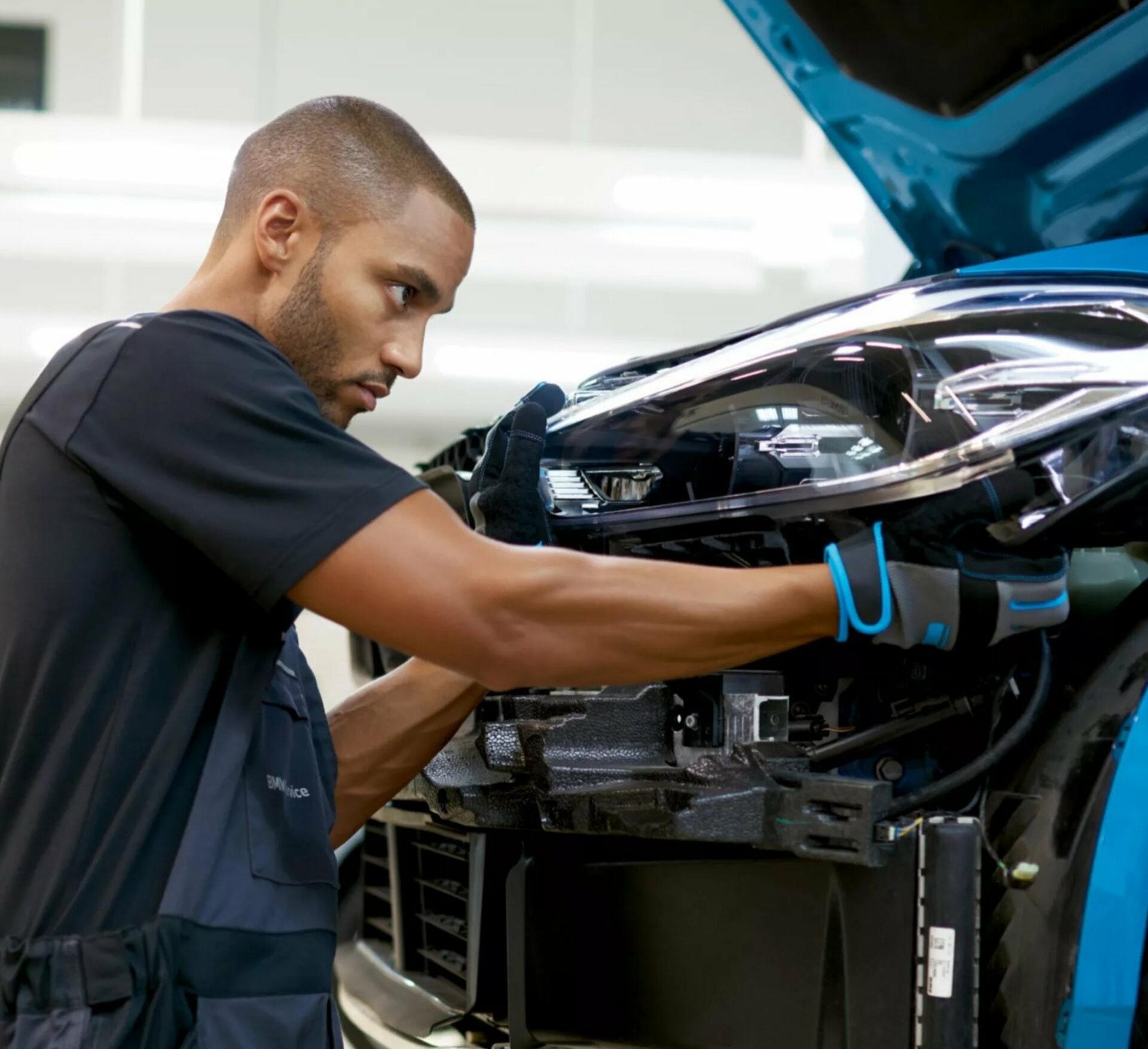 Ein Mitarbeiter aus einer BMW Werkstatt repariert einen türkisfarbenen BMW.