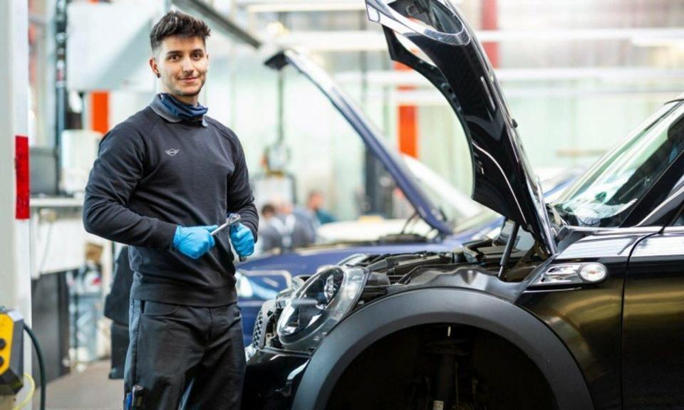 Ein Servicemitarbeiter einer MINI Werkstatt steht mit einem Schraubenschlüssel vor der geöffneten Motorhaube eines MINI.