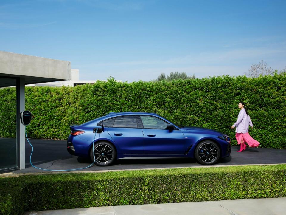 Ein BMW i4 M50 xDrive Gran Coupé in der Lackierung "Individual Frozen Portimao Blue metallic" lädt an einer Wallbox.