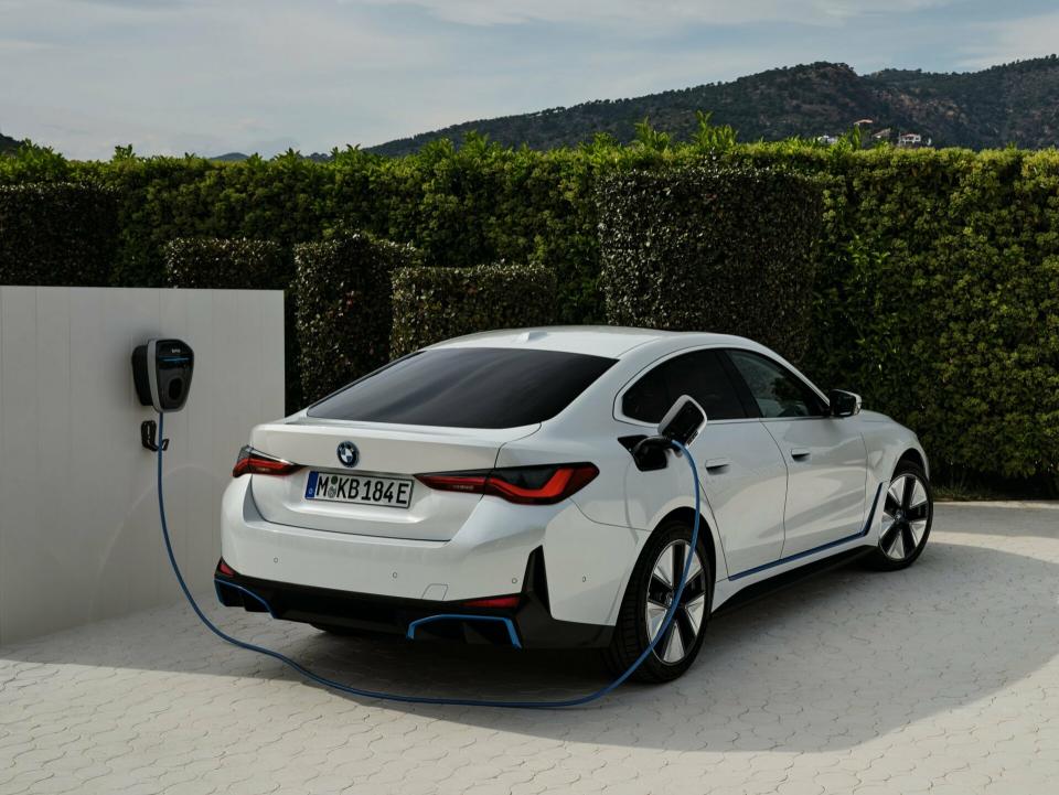 Ein weißer BMW i4 wird an einer Wallbox aufgeladen. Im Hintergrund ist ein Gebirge.
