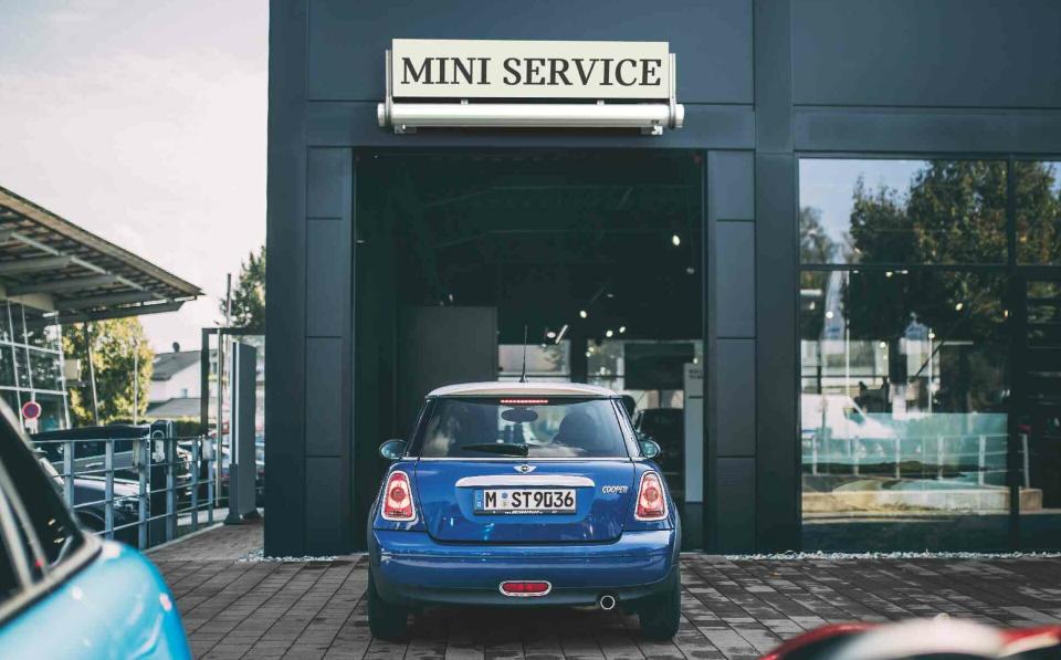 Ein blauer MINI Cooper steht auf dem Parkplatz vor dem Eingang einer MINI Service Werkstatt.