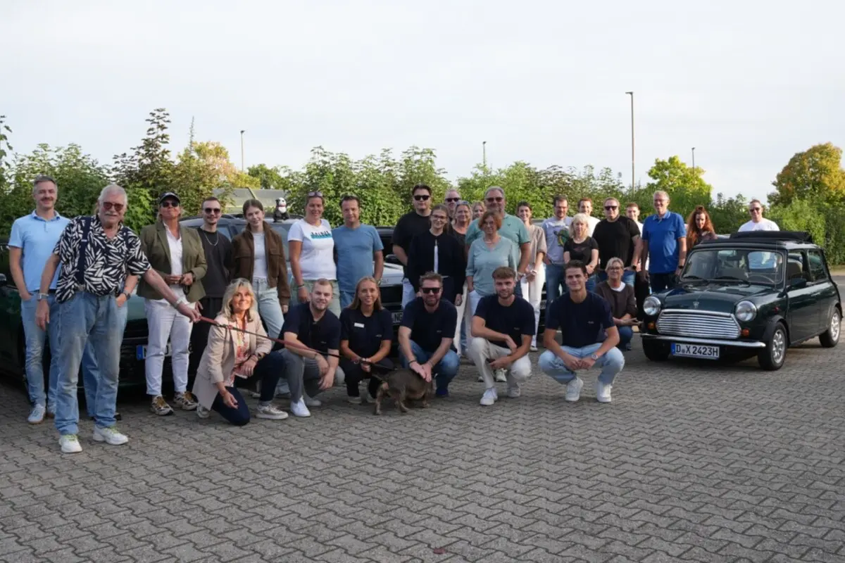 Ein Gruppenfoto der Teilnehmer der MINI Ausfahrt des Autohauses Fett & Wirtz mit einem original MINI Cooper Oldtimer.