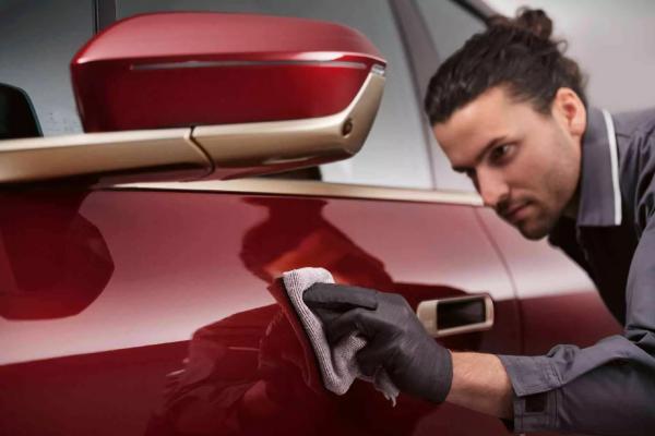 Ein Mitarbeiter einer BMW Werkstatt poliert den Lack eines roten BMW mit einem Microfastertuch,