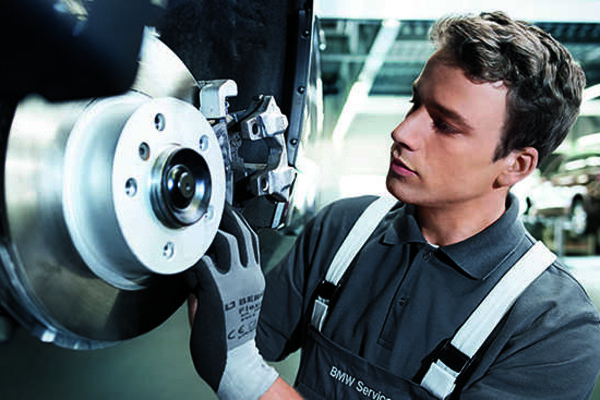 Ein Mitarbeiter des BMW Service eines Autohauses prüft kritisch eine Bremsanlage eines BMW Fahrzeuges.