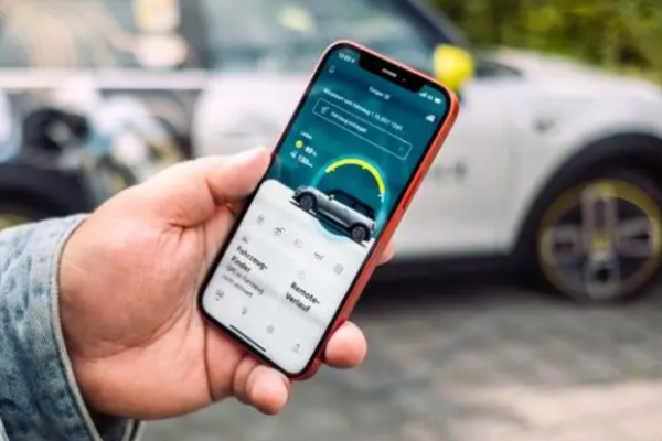 Ein Mann betrachtet in der Hand sein Smartphone mit der MINI App. Im Hintergrund steht sein MINI Cooper.