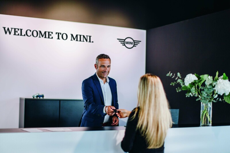 Ein Mitarbeiter in einem MINI Autohaus übergibt einer jüngeren, interessierten Kundin ihren Autoschlüssel..