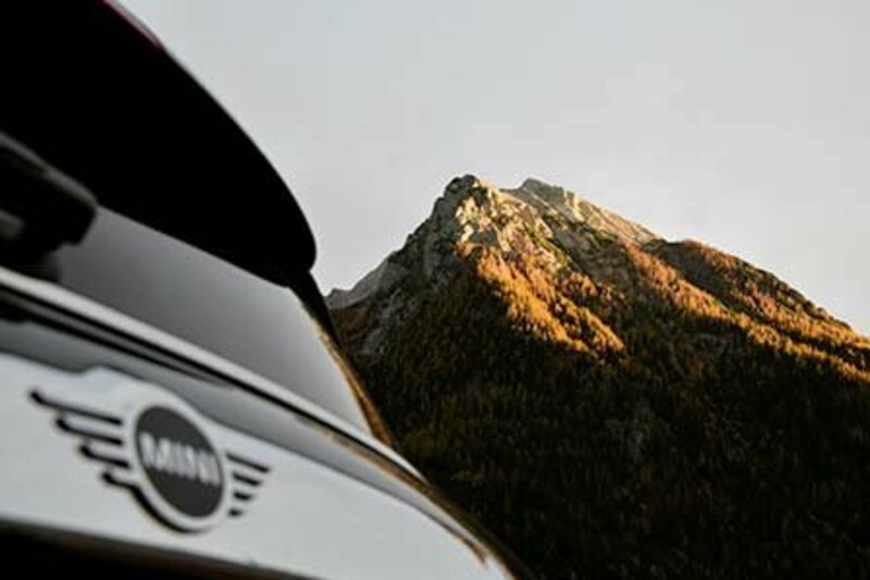 Das Heck eines schwarzen MINI Coopers. Im Hintergrund steht der sonnige Gipfel eines Berges.