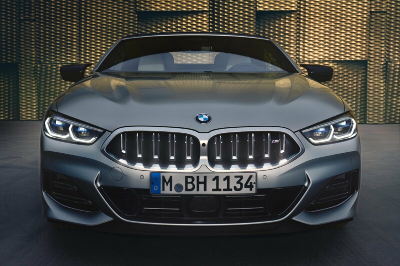 Der Kühlergrill eines BMW M850i Cabriolets in der FarbeSkyscraper Grau metallic vor einer modernen, goldenen Fassade.