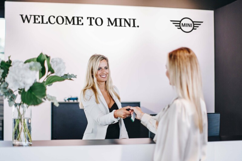 Eine Mitarbeiterin in einem MINI Autohaus übergibt einer jüngeren, interessierten Kundin ihren Autoschlüssel..