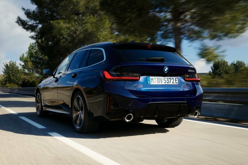 Der BMW 330e Touring auf einer bewaldeten Landstraße im Sonnenschein.