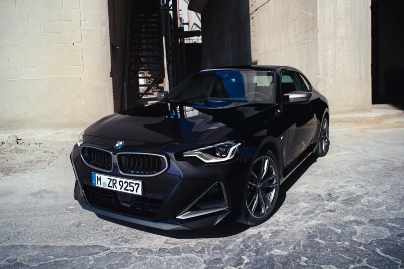 Ein BMW M240i xDrive M Performance in der Farbei thundernight metallic parkt an einem Betongebäude.