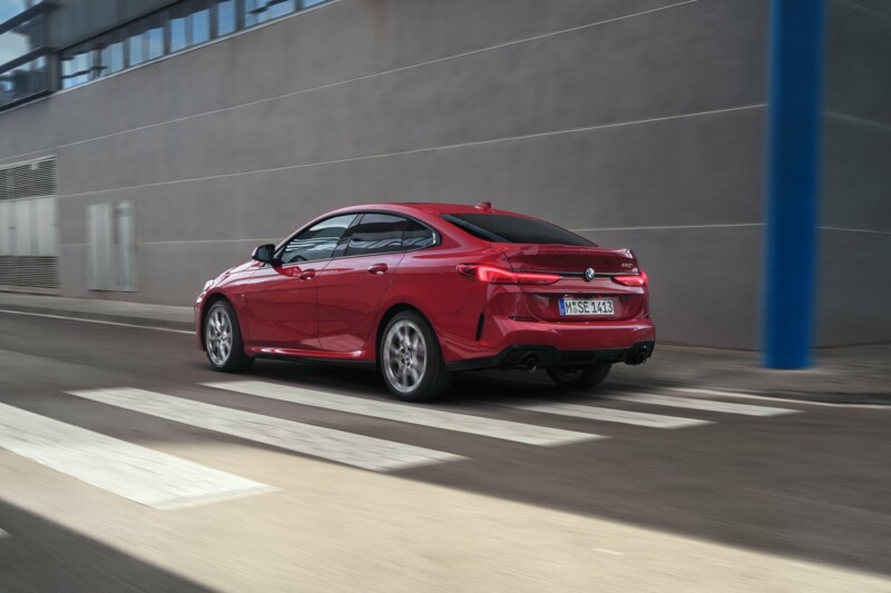 Ein BMW 220i Gran Coupé in der Farbe fire red metallic fährt an einem modernen Gebäude entlang.