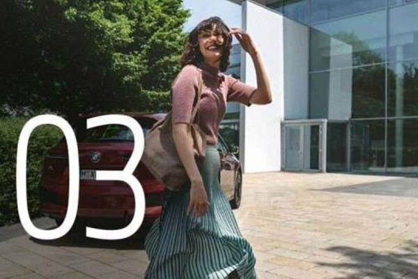 Nummer 3: Eine Dame in einem grünen Kleid läuft in ein Firmengebäude mit Glasfassade. Im Hintergrund ein dunkelroter BMW iX.