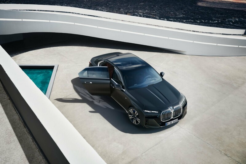 Eine schwarze BMW 740i Limousine neben einem Brunnen an einem modernen Gebäude.