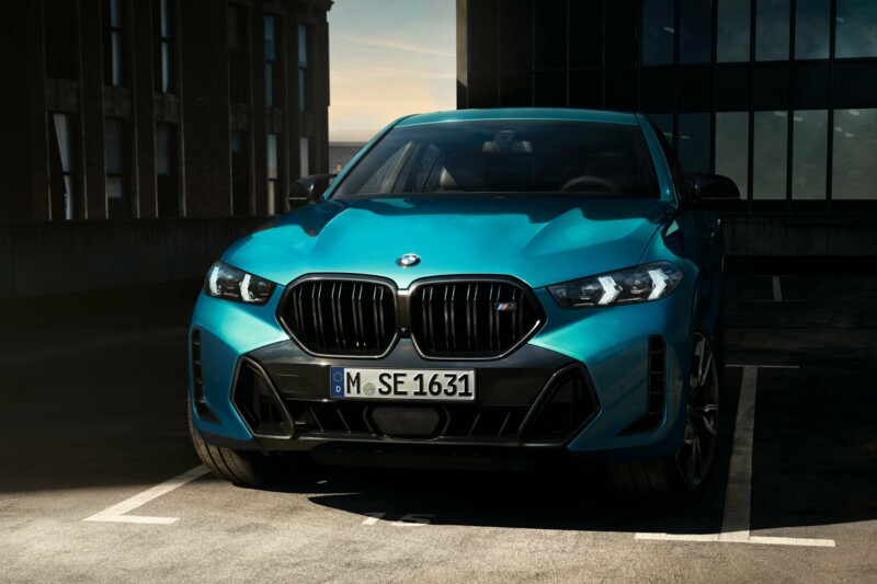 Ein BMW X6 M Competition in der Farbe M Isle of Man Grün metallic in einer Parkbucht an einem Metall-Tor.