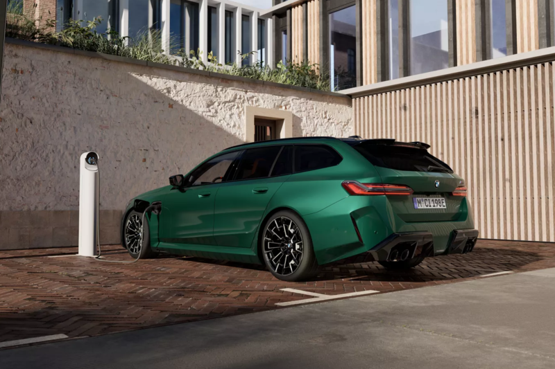 Das Heck eines BMW M5 Touring in M Isle of Man grün an einer Ladestation vor einem Gebäude.
