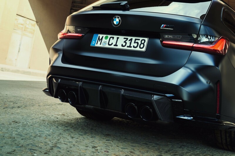 Die Heckansicht eines BMW M3 Competition M xDrive an einem Industriegebäude.
