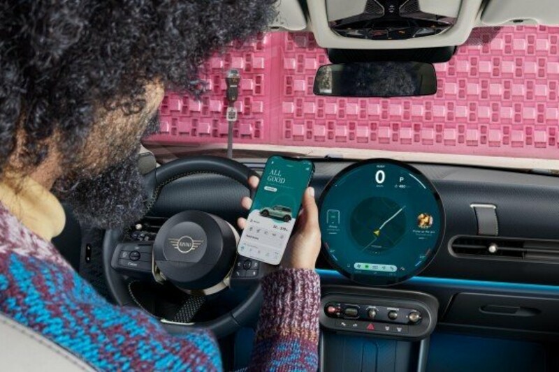 Ein Mann sitzt in seinem MINI Cooper 3-Türer und bedient die MINI App auf seinem Smartphone.